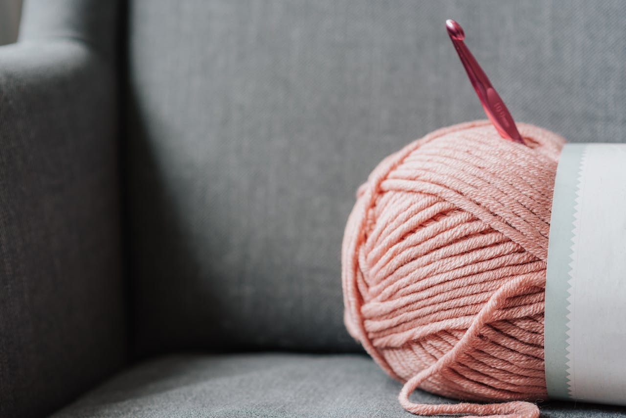 Close-up of pink yarn with a crochet hook resting on a cozy couch, perfect for DIY crafts.