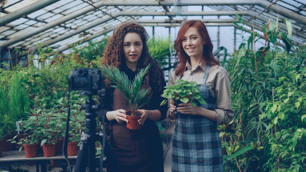 pexels photo 36729348 36729348 Two women in a greenhouse filming a video tutorial on plant care. Vibrant greenery surrounds them.